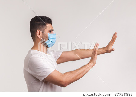 Side view of alarming man in hygienic protective mask gesturing stop, afraid of coronavirus infection, respiratory illnesses such as flu, 2019-nCoV. indoor studio shot isolated on white background Side view of alarming man in hygienic protective mask gesturing stop, afraid of coronavirus infection, respiratory illnesses such as flu, 2019-nCoV. indoor studio shot isolated on white background 87738885