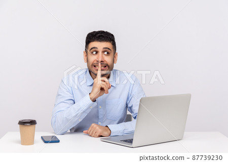 Please, be quiet. Funny positive man employee sitting office workplace with laptop, asking for silence or secrecy, keeping finger on lips and hushing, confidential information. studio shot isolated 87739230