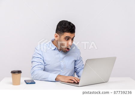 Oh my god, wow. Amazed businessman sitting office workplace looking at laptop screen with surprised expression, talking on video call, reading shocking news. studio shot isolated on white background 87739236