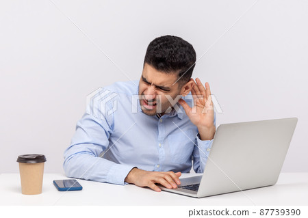 Confused businessman sitting office workplace, leaning towards laptop and holding hand near ear trying to hear better, listening for quiet noise. indoor studio shot isolated on white background Confused businessman sitting office workplace, leaning towards laptop and holding hand near ear trying to hear better, listening for quiet noise. indoor studio shot isolated on white background 87739390