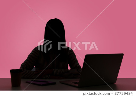 Female silhouette working on laptop sitting at workplace in dark office, shadow business, corruption, night shift. Indoor studio shot isolated on pink background 87739484