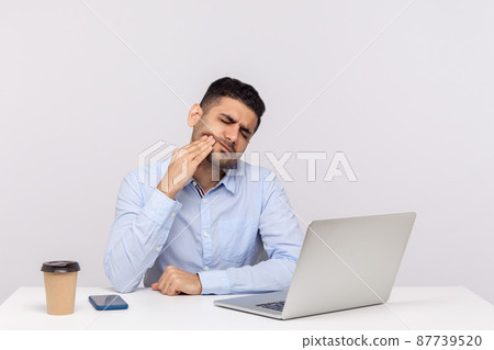 Sudden dental problems at work. Unhealthy man employee sitting in office, touching painful cheek, suffering acute toothache, inflamed gums, cavities or tooth decay. indoor studio shot isolated 87739520