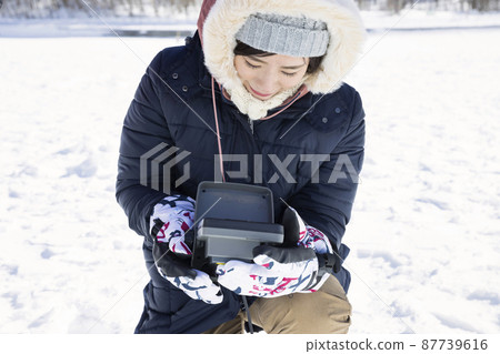 年輕女子在冰上釣魚的圖像看著魚探儀 年輕女子在冰上釣魚的圖像看著魚探儀 87739616