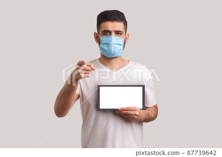 StayAtHome. Man in protective mask holding Stay at home inscription and pointing to camera, warning of coronavirus quarantine, Covid-19 epidemic, preventive measures for spread of infectious disease. StayAtHome. Man in protective mask holding Stay at home inscription and pointing to camera, warning of coronavirus quarantine, Covid-19 epidemic, preventive measures for spread of infectious disease. 87739642