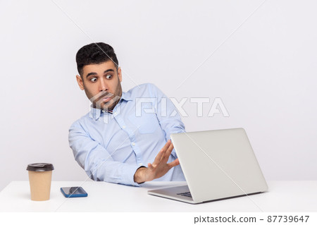 Scared frightened man employee sitting office workplace, showing stop to laptop screen with video call, looking terrified, afraid to watch horror content. studio shot isolated on white background Scared frightened man employee sitting office workplace, showing stop to laptop screen with video call, looking terrified, afraid to watch horror content. studio shot isolated on white background 87739647