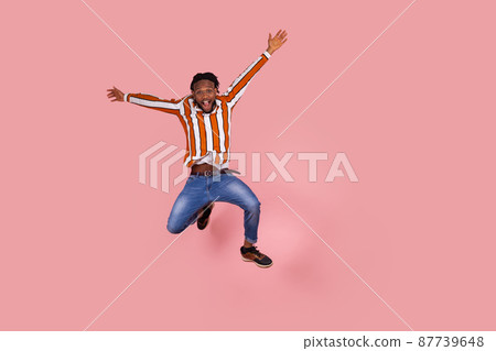 Excited afro-american man with dreadlocks highly jumping and rising hands, pretending he is flying, looking at camera with satisfied surprised expression. Indoor studio shot isolated on pink Excited afro-american man with dreadlocks highly jumping and rising hands, pretending he is flying, looking at camera with satisfied surprised expression. Indoor studio shot isolated on pink 87739648