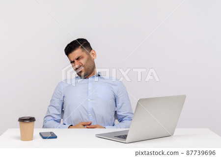 Sudden stomach ache at work. Unhealthy man employee sitting in office, suffering heartburn, gastrointestinal disorder, symptoms of constipation indigestion. studio shot isolated on white background 87739696
