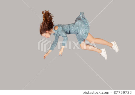 Hovering in air. Relaxed beautiful girl ruffle dress and curly soaring hair levitating, flying in dream with hands up, reaching for something high. indoor studio shot isolated on gray background 87739723