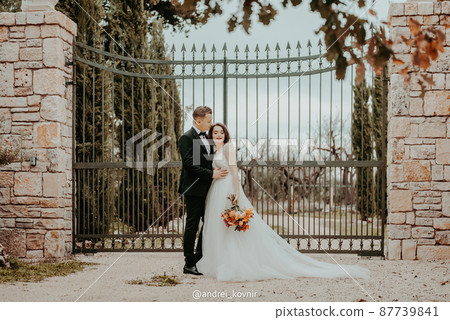 Happy stylish smiling couple walking in Tuscany, Italy on their wedding day. The bride and groom walk down the street by the hands. A stylish young couple walks. Husband and wife communicate nicely Happy stylish smiling couple walking in Tuscany, Italy on their wedding day. The bride and groom walk down the street by the hands. A stylish young couple walks. Husband and wife communicate nicely 87739841
