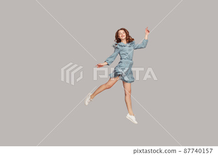 Happy delicate girl in vintage ruffle dress levitating with ballet dance move, hovering in mid-air and smiling joyfully, jumping trampoline, flying up. indoor studio shot isolated on gray background 87740157