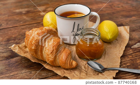 Lemon tea, home made jam, croissant on wooden table. Breakfast concept. 87740168