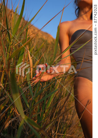young beautiful woman in a halter swimsuit walks along the beach at sunset 87742028