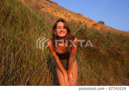 young beautiful woman in a halter swimsuit walks along the beach at sunset 87742029