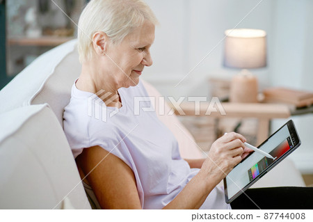 elderly woman sitting in a yoga pose in front of an open laptop. elderly woman sitting in a yoga pose in front of an open laptop. 87744008