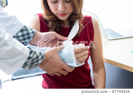 man doctor with wrapping nurse bandages splint to the arm of a female patient wear arm splint with analogue pressure gauge for better healing In the room hospital background. 87744836