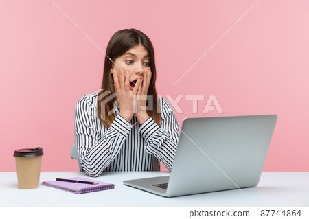 Extremely shocked surprised woman office worker looking at laptop display with big eyes and open mouth, confused with information. Indoor studio shot isolated on pink background 87744864