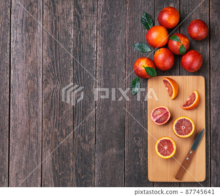 Sliced and whole ripe red oranges on a wooden cutting board top view. 87745641