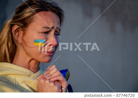 War portrait of Ukrainian woman with national flag on cheek crying 87746720