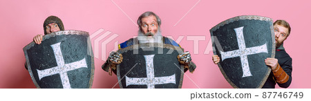 Three mix-aged men, medieval warriors in armor hiding themselves behind a shield isolated over pink studio background. Look scared. Collage Three mix-aged men, medieval warriors in armor hiding themselves behind a shield isolated over pink studio background. Look scared. Collage 87746749