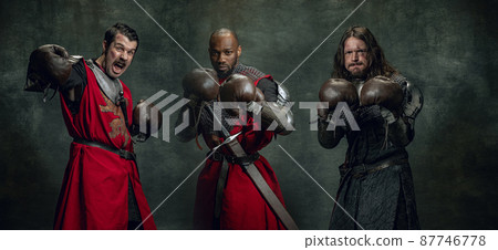 Portraits of medieval warriors or knights with dirty wounded face in boxing gloves isolated over dark background. Comparison of eras, history, sport Portraits of medieval warriors or knights with dirty wounded face in boxing gloves isolated over dark background. Comparison of eras, history, sport 87746778