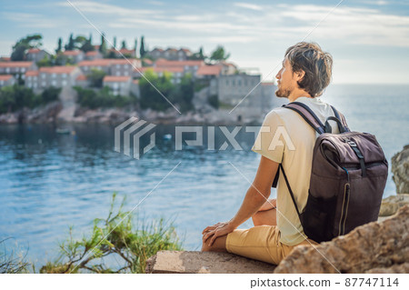 Man tourist on background of beautiful view of the island of St. Stephen, Sveti Stefan on the Budva Riviera, Budva, Montenegro. Travel to Montenegro concept 87747114