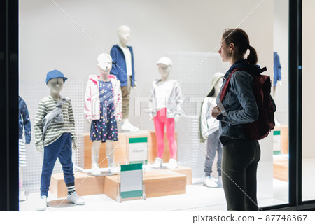 Woman stands outside the children's store and looks at the clothes on the mannequins. 87748367