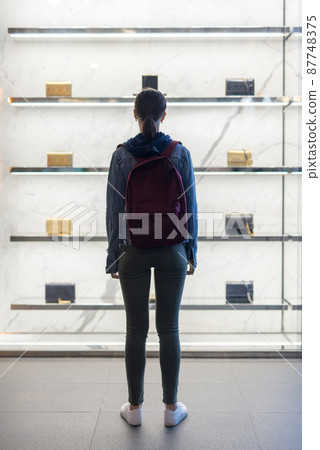 Woman stands in front of a store window with bags 87748375