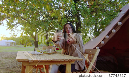 Mom and daughter sit at a wooden table in nature and take a selfie on the phone. Family on a picnic. Mom and daughter sit at a wooden table in nature and take a selfie on the phone. Family on a picnic. 87748817