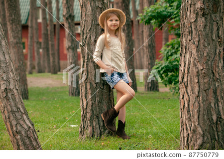 Smiling tween girl leaning against tall tree in courtyard of country house in summer 87750779