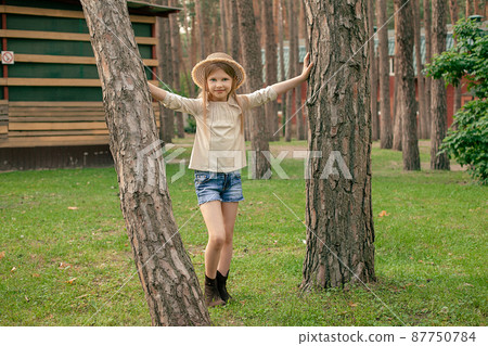 Smiling tween girl standing touching on two trees in green summer courtyard of country house 87750784