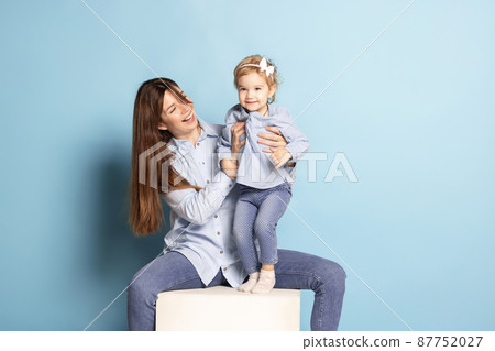 Studio shot of beautiful happy woman and little kid, mother and daughter isolated on blue background. Mother's Day celebration. Concept of family, childhood Studio shot of beautiful happy woman and little kid, mother and daughter isolated on blue background. Mother's Day celebration. Concept of family, childhood 87752027