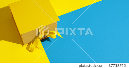 Bright yellow gift box with ribbon bow on yellow and blue  background top view copy space. Birthday present, March 8, Mothers Day, Valentines Day, Easter or spring concept. 87752753