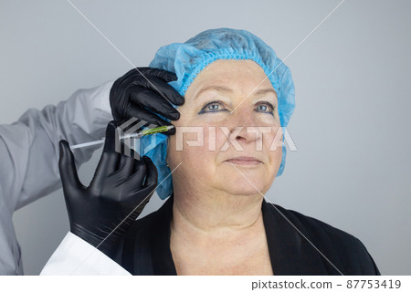 Botulinum toxin injection. Senior woman at the appointment with a beautician who is preparing to give anti-wrinkle injections. Loose skin and hypotension. Mimic wrinkles and contouring Botulinum toxin injection. Senior woman at the appointment with a beautician who is preparing to give anti-wrinkle injections. Loose skin and hypotension. Mimic wrinkles and contouring 87753419