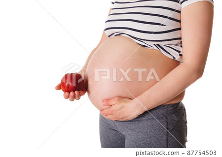 Pregnant woman standing and holding apple near her stomach 87754503