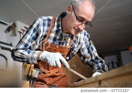 Carpenter filing a plank of wood in his Workshop. 87755287