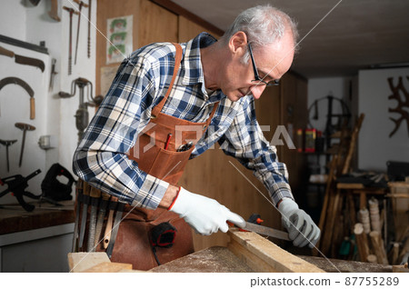 Carpenter filing a plank of wood in his Workshop. 87755289