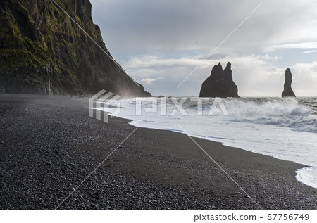 The famous Black Sand ocean Beach, mount Reynisfjall and Picturesque Basalt Columns, Vik, South Iceland. People unrecognizable. The famous Black Sand ocean Beach, mount Reynisfjall and Picturesque Basalt Columns, Vik, South Iceland. People unrecognizable. 87756749