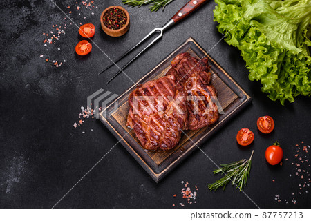Grilled ribeye beef steak, herbs and spices on a dark table Grilled ribeye beef steak, herbs and spices on a dark table 87757213