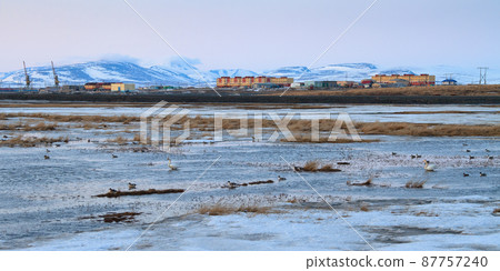 Spring arctic landscape. View of the river in the tundra, colorful buildings and mountains. Beautiful evening panorama Spring arctic landscape. View of the river in the tundra, colorful buildings and mountains. Beautiful evening panorama 87757240