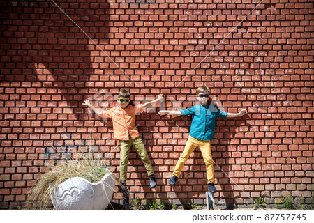 Two teenage boys sibling brothers with sunglasses in casual clothes are looking at camera and smiling, standing against yellow brick wall. Friendship concept 87757745