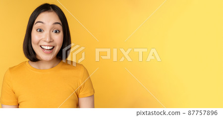 Close up portrait of asian girl showing surprised reaction, raising eyebrows amazed, reacting to big news, standing over yellow background Close up portrait of asian girl showing surprised reaction, raising eyebrows amazed, reacting to big news, standing over yellow background 87757896