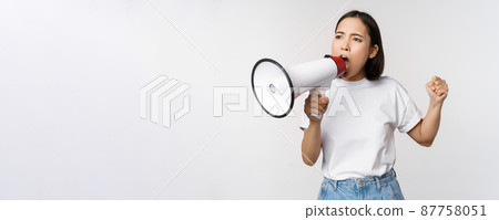Asian girl shouting at megaphone, young activist protesting, using loud speakerphone, standing over white background Asian girl shouting at megaphone, young activist protesting, using loud speakerphone, standing over white background 87758051