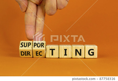Directing or supporting leadership style symbol. Businessman turns cubes, changes words supporting to directing. Beautiful orange background, copy space. Business, directing or supporting concept. Directing or supporting leadership style symbol. Businessman turns cubes, changes words supporting to directing. Beautiful orange background, copy space. Business, directing or supporting concept. 87758316