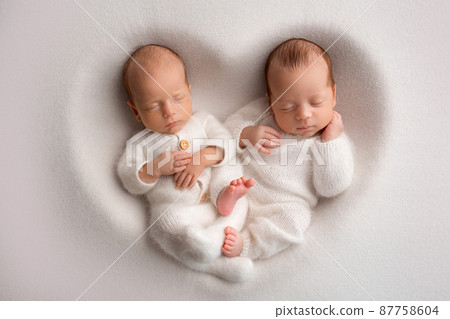 Tiny newborn twin boys in white bodysuits on a white background. Newborn twins sleep next to their brother on the background of the heart. Two newborn twin boys hugging each other. Tiny newborn twin boys in white bodysuits on a white background. Newborn twins sleep next to their brother on the background of the heart. Two newborn twin boys hugging each other. 87758604