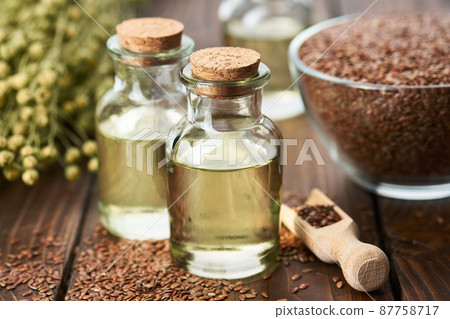 Two bottles of fresh linseed oil and glass bowl of whole flax seeds. Bundle of linen flax plants on table. Two bottles of fresh linseed oil and glass bowl of whole flax seeds. Bundle of linen flax plants on table. 87758717
