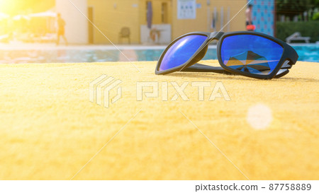 Sunglasses pool summer background. Beach pool equipment with travel sunglasses on yellow holiday towel. Sun glasses near swimming pool, holiday concept. 87758889