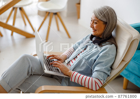 Cheerful woman using modern laptop at home 87761800