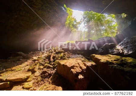 Cave opening with beams of light shining in 87762192