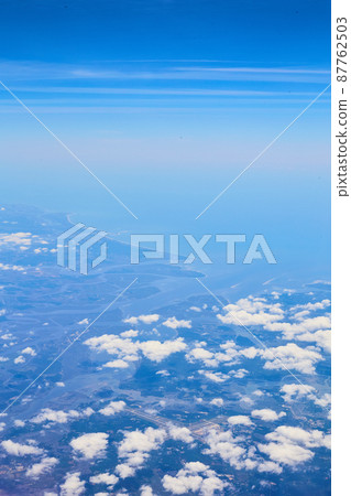 Airplane view of clouds and blue sky with land in distance Airplane view of clouds and blue sky with land in distance 87762503