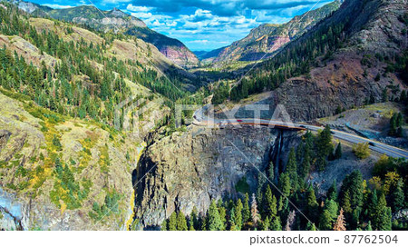 Valley in mountains with small road curving through and waterfall Valley in mountains with small road curving through and waterfall 87762504